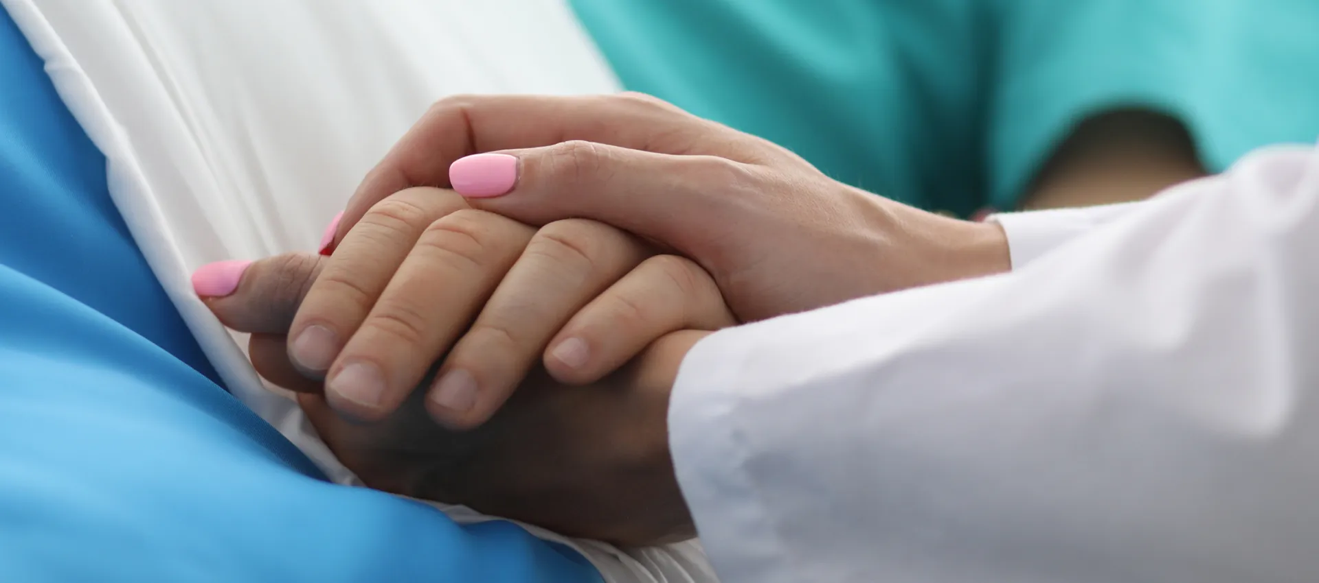 Close-up of hands clasped in a comforting gesture between a patient and a medical professional, with blue scrubs in the background.