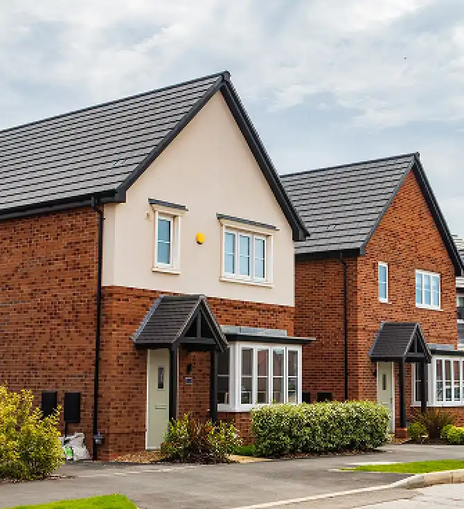 Two attached brick houses with pitched roofs, cream panels, small entry porches, neatly trimmed shrubs, and a clear blue sky.